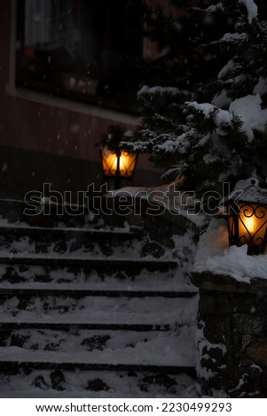 Dark but hygge and cozy winter mood in Italian snowy mountain village ski resort. Noir style, white snow and orange lights, yellow christhmas light