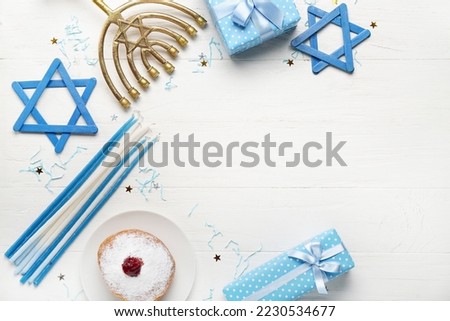 Frame made of plate with tasty doughnut, gifts and decor for Hanukkah celebration on white wooden background