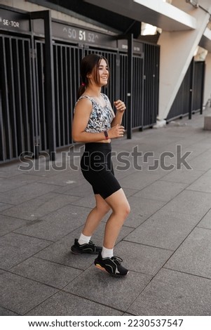 Teenage girl doing sports warm-up and wrestling exercises on the street against the city background