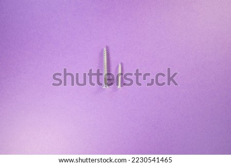 one small and one large new unused silver screws isolated on a purple background