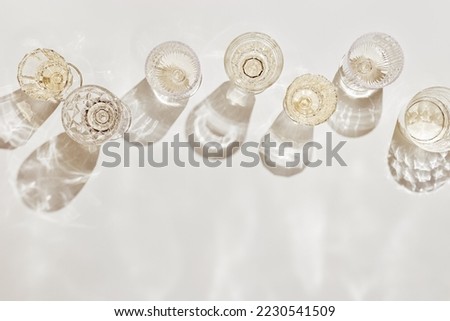 Top view white sparkling wine in different glasses of wine, stemmed glass with sun shadow and glare on light beige background. White wine tasting concept flat lay, copy space. Summer alcoholic drinks