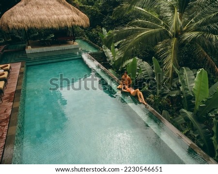 Aerial shot of man and woman relaxing at the poolside. Couple enjoying holiday at luxury resort.