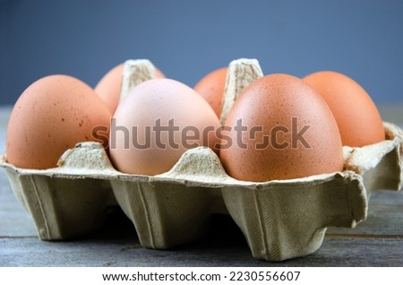 Six brown chicken eggs in box on wooden table, blue background