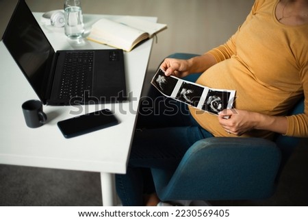 Beautiful young pregnant woman looking at ultrasound pictures of her baby. Businesswoman in office