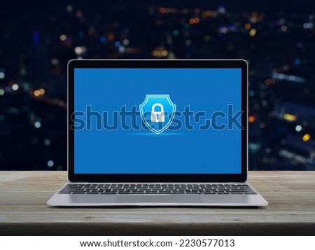 Padlock with shield flat icon on modern laptop computer monitor screen on wooden table over blur colorful night light city tower and skyscraper, Technology security insurance online concept
