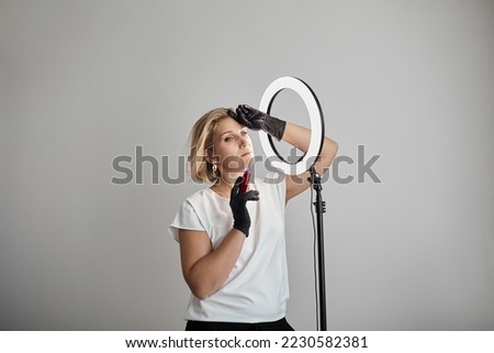 Beautician with permanent makeup machine on grey background. Woman with permanent machine in hand, Cosmetic Tattoo tool, ring light. Beauty blogger