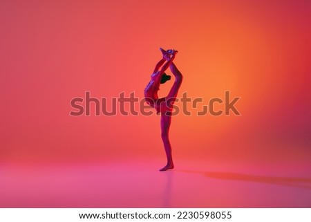 Stretching. Young flexible teen girl rhythmic gymnast in motion, action isolated over pink background in neon light. Sport, beauty, competition, flexibility, active lifestyle. Individual performance