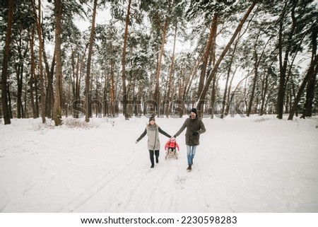 Father, mother, and child in children's sled walk and play in the park. Happy family with kid having fun in winter forest. Mom, dad, daughter running and walking in snow in mountains. Winter holidays.