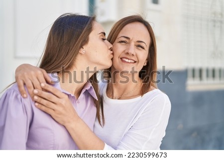 Two women mother and daughter hugging each other and kissing at street