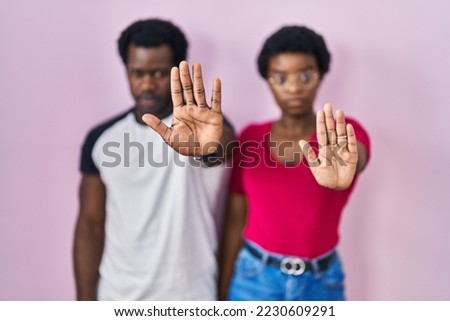 Young african american couple standing over pink background doing stop sing with palm of the hand. warning expression with negative and serious gesture on the face. 