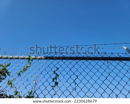 The top of a fence under a blue sky as barbed wire runs across it.
