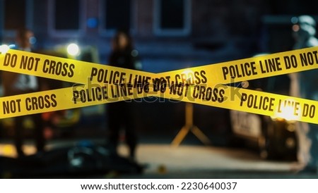 Restricted Area: Yellow Tape Showing Text "Police Line Do Not Cross". Blurred Background with Crime Scene Investigation Squad Working on a Murder Case at Night. Cinematic Aesthetic Shot Royalty-Free Stock Photo #2230640037
