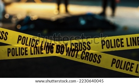 Shot Focused on Yellow Tape Showing Text "Police Line Do Not Cross". Tape Used to Restrict a Crime Scene Where Forensics, Detectives and Policemen are Working on Solving a Homicide Case Royalty-Free Stock Photo #2230640045