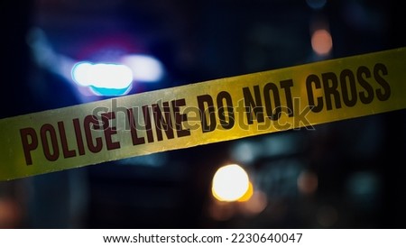 Close Up Shot Focused on Yellow Tape Showing Text "Police Line Do Not Cross". Tape Used to Restrict a Crime Scene. Bokeh Background with Flickering Blue Siren Lights