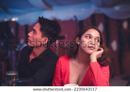 A couple having a date at an elegant restaurant sits back to back and ignores each other as they are having an argument. A lady is upset with her insensitive boyfriend. Waiting for the night to end. Royalty-Free Stock Photo #2230643517