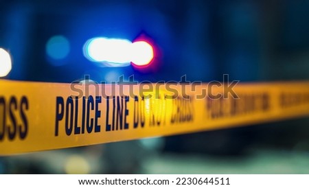 Close Up Shot Focused on Yellow Tape Showing Text "Police Line Do Not Cross". Restricted Area of a Crime Scene. Bokeh Background with Flickering Siren Lights. Forensics Team Working on a Case Royalty-Free Stock Photo #2230644511