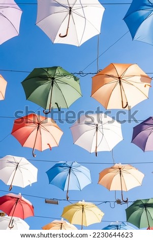 Open multi-colored umbrellas hang over passage between houses. Abstract colorful background