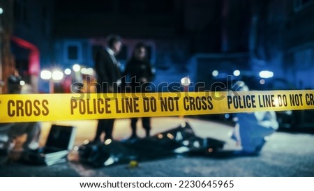 Close Up on Crime Scene Yellow Tape Showing Text "Police Line Do Not Cross". Restricted Area to the Public. Police on Duty in the Background. Cinematic Bokeh Effect With Red and Blue Neon Lights Royalty-Free Stock Photo #2230645965