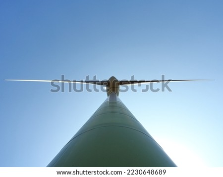 A closeup undershot of a wind turbine against a clear sky background