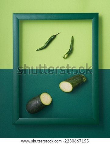 Whole and chopped chili peppers and zucchini in wooden picture frame on two-tone green background