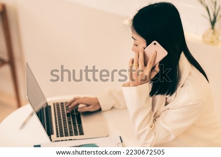 Female Entrepreneur. Asian Businesswoman Talking On Phone Working On Laptop In Modern Office. Empty Space