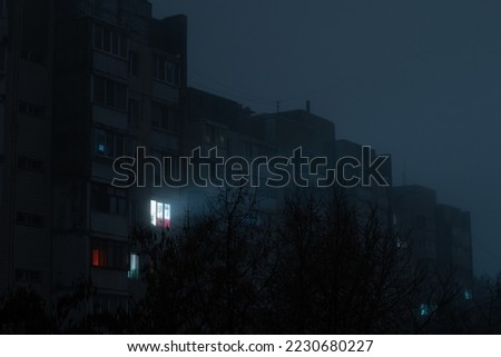 Light in one window in apartment multistorey building in fog during blackout of electricity in a residential area of Kyiv after russian shelling of power plants. Royalty-Free Stock Photo #2230680227