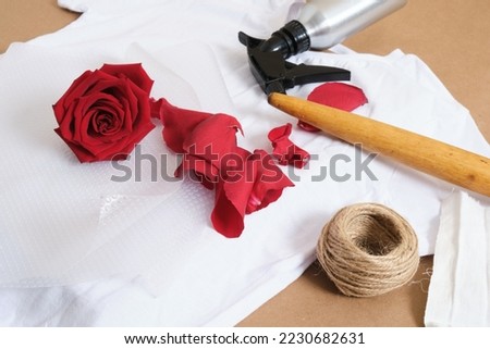 eco print concept kit for dyeing a t-shirt with a rose flower press, a spray with a fixative, water and a rolling pin, rose petals are imprinted and dye the fabric