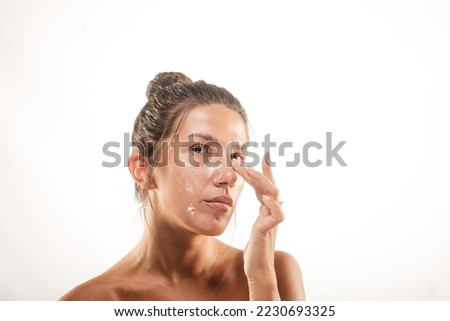 Close up of a beautiful girl smearing the face cream at the studio on a white backround