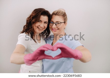 Portrait of two qualified cosmetologists-women, confidently smiling and making a heart with their hands in a medical center.