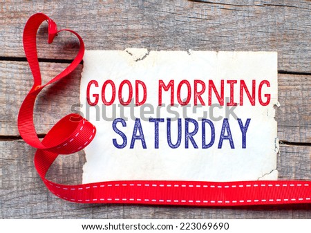 Good Morning Saturday. White card with text Good Morning Saturday on wooden table, with red ribbon 