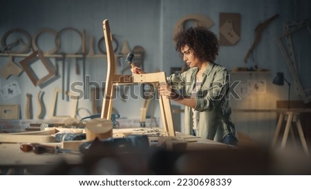 Young Woodworker Checking the Layout Manual of a Stylish Handmade Wooden Chair. Talented Female Furniture Designer Working in a Workshop in a Creative Loft Space with Tools and Equipment. Royalty-Free Stock Photo #2230698339