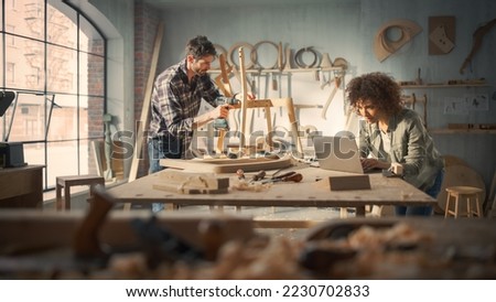 Small Business Owners of a Furniture Store Working on a New Wooden Dining Table Chair. Carpenter Building the Chair, While Young Female Manager Using Laptop Computer.