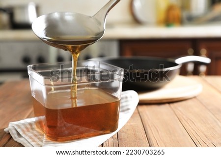Pouring used cooking oil with ladle into container on wooden table in kitchen Royalty-Free Stock Photo #2230703265
