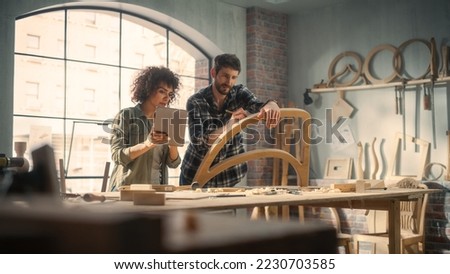 Small Business Owners of a Furniture Workshop Using Tablet Computer and Discussing the Design of a New Wooden Chair. Handsome Carpenter and Young Female Apprentice Working in Loft Studio.