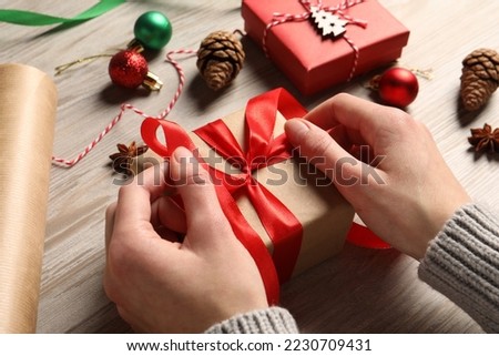 Woman decorating gift box on white wooden table, closeup. Christmas present