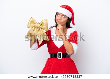 Young hispanic woman dressed as mama noel holding a Christmas bow isolated on white background having doubts