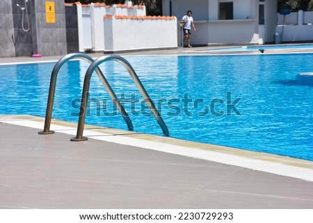 Close up shot of a blue color swimming pool with metal ladder. Modern swimming pool	