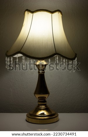 A vintage lampshade in front of a gray wall and on a white table. Golden yellow colour retro desk lamp. Royalty-Free Stock Photo #2230734491