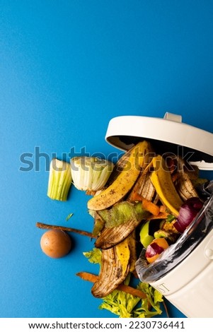 Vertical image of organic fruit and vegetable food waste spilling from open kitchen composting bin. On blue background with copy space. Ecology, recycling, care and nature concept. Royalty-Free Stock Photo #2230736441