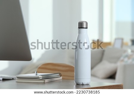 Stylish thermo bottle on wooden table at workplace in office Royalty-Free Stock Photo #2230738185