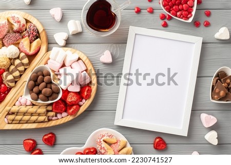 Valentine's Day concept. Top view photo of photo frame wooden heart shaped serving tray glass of drinking plates with sweets candies and cookies on grey wooden table background with copyspace