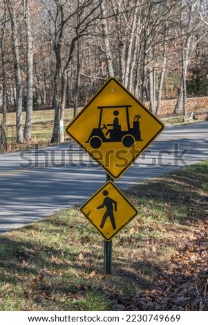 Two signs on a pole alongside the street by a golf course and trails showing a golf cart and pedestrian crossing ahead to approach with caution closeup view