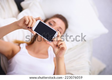 Happy woman taking a photo of herself with her mobile phone in a bedroom
