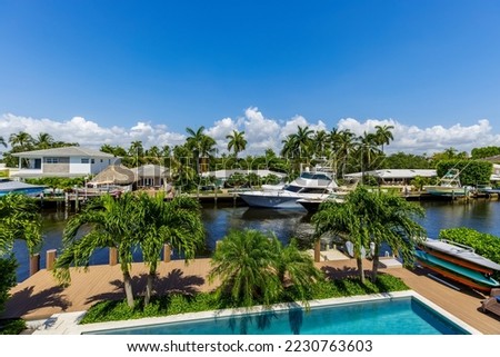 View from balcony to canal with boats in Miami neighborhood, with abundant vegetation, palms and tropical plants, swimming pool, white railing