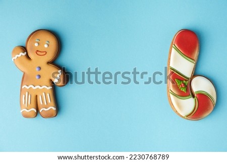 Gingerbread man decorated with white icing and candy cane isolated on the blue pastel background. Flat lay. Traditional homemade Christmas cookies. Copy space