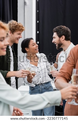 Smiling multiethnic business people talking and holding champagne during corporative party