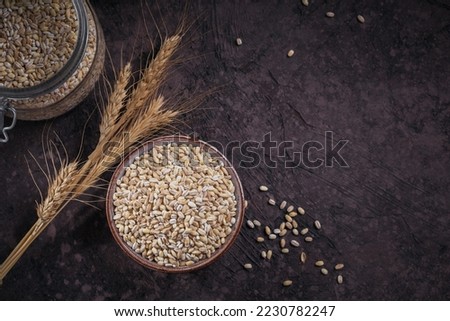 Bowl of dry raw broken pearl barley cereal grain on dark background. Cooking pearl barley porridge concept. Royalty-Free Stock Photo #2230782247