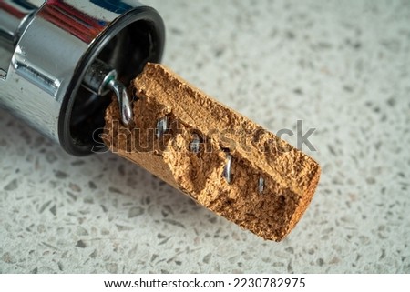 Damaged wine cork that has broken off with the shiny corkscrew a visible metal spiral down the middle. The brown cork is fractured and fragmented. Laying on a grey speckled laminate kitchen surface.  Royalty-Free Stock Photo #2230782975