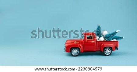 The red car is carrying green Christmas trees in the back. Christmas card with copy space on a blue background. High quality photo