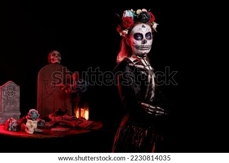 Horror skull make up on glamorous model to celebrate dios de los muertos mexican tradition, posing on holiday celebration. Lady of death with la cavalera catrina costume and body art.